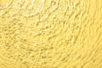 Rippled surface of clear water on yellow background, closeup