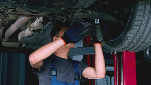 Young male mechanic repairing car suspension, standing under vehicle at garage, slow motion