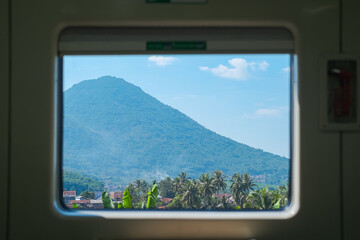A breathtaking view of a mountain framed by a train window on a West Java route, with clear blue skies and lush greenery, capturing the beauty of Indonesia’s natural landscapes