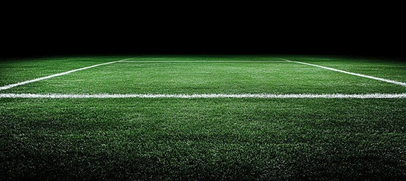 A close-up of a white line on a green grass field with dark background.