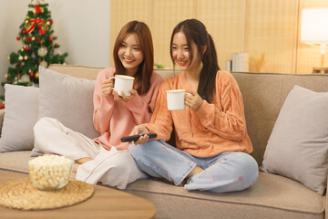 Friendship concept, LGBT lesbian couple drinking coffee and switching channel while watching movie