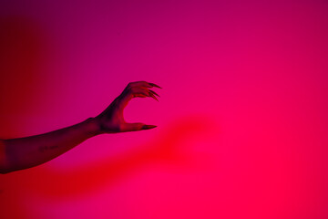 A terrifying witch's hand with long red nails, resembling a demon or vampire. Its gnarled appearance hints at monstrous origins, resembling an alien or ghostly entity,with zombie-like decayed skin.