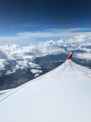 Aerial view from airplane window during flight over mountains, cloudy valley, and wing in sight, capturing the freedom of air travel, high altitude, and stunning nature below