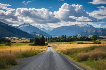 Naklejka premium Asphalt road winds through green fields and hills to rugged mountains in New Zealand. Rolling countryside stretches to majestic peaks. Clouds drift lazily across the sky.