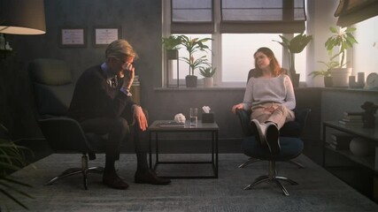 Upset woman sits in chair during counseling session with psychologist. Mature therapist talks to depressed patient, asks questions, provides cognitive behavioral therapy. Psychology and mental health.