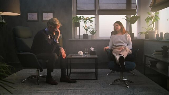 Upset woman sits in chair during counseling session with psychologist. Mature therapist talks to depressed patient, asks questions, provides cognitive behavioral therapy. Psychology and mental health.
