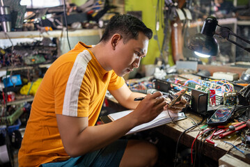 Repair man looks at the circuit and takes notes on the workbench at the service station.