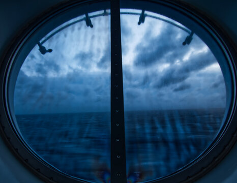 view of the ocean on a dark cloudy day from a porthole window on a cruise ship
