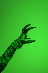A bloodied witch hand wrapped in bandages, set against a green fire background. This demonic hand...