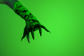 A bloodied witch hand wrapped in bandages, set against a green fire background. This demonic hand...