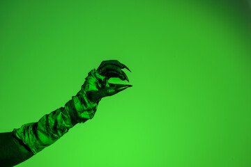 A bloodied witch hand wrapped in bandages, set against a green fire background. This demonic hand...