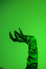 A bloodied witch hand wrapped in bandages, set against a green fire background. This demonic hand...