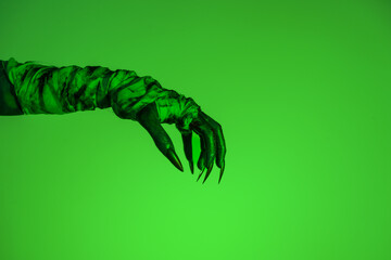 A bloodied witch hand wrapped in bandages, set against a green fire background. This demonic hand...