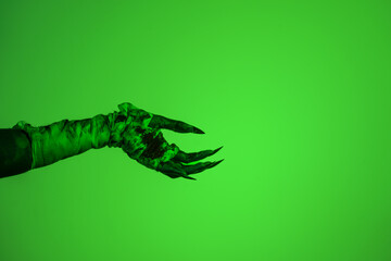 A bloodied witch hand wrapped in bandages, set against a green fire background. This demonic hand...