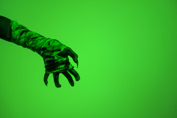A bloodied witch hand wrapped in bandages, set against a green fire background. This demonic hand...