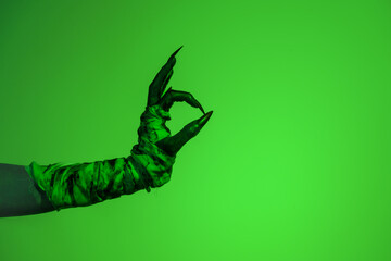 A bloodied witch hand wrapped in bandages, set against a green fire background. This demonic hand...