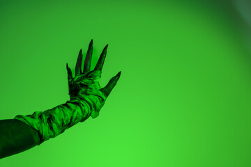 A bloodied witch hand wrapped in bandages, set against a green fire background. This demonic hand...