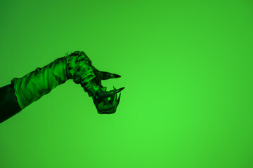 A bloodied witch hand wrapped in bandages, set against a green fire background. This demonic hand...