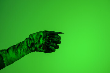 A bloodied witch hand wrapped in bandages, set against a green fire background. This demonic hand...