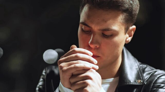 Outdoor portrait of serious guy smoking at night park, slow motion, looking pensively at camera, slow motion