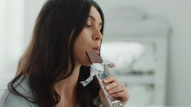Seizing stress. Close up portrait of young depressed woman eating chocolate, biting bar at home, slow motion