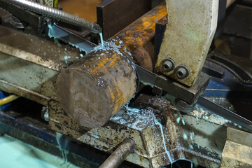 Industrial bandsaw automated machine cutting metal detail with coolant pouring from pipe. Metalworking metallurgical industry, automated machinery production manufacturing. Cut metal cylinder.