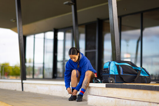 footballer sitting on step tying boot laces with kit bag alongside