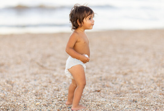 little aboriginal toddler wearing only a nappy on the beach with quizzical look on face