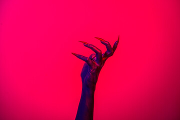A witch hand with long nails appears against a red fire background, evoking a demonic, monstrous...