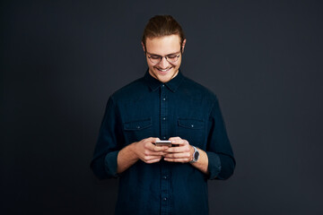 Man, employee and happy in studio with smartphone for social media post and interaction on dark background. Male person, texting and smile or satisfied with message notification and communication