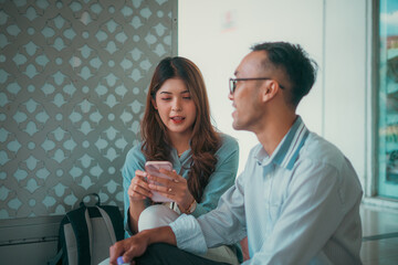 Obraz premium A man and a woman are sitting comfortably on the floor together, both focused intently on the same cell phone as they explore it