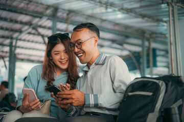A man and a woman are sitting closely next to each other while intently looking at the screen of a cell phone they are sharing together
