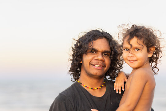 aboriginal teenager holding young sibling against pale sky