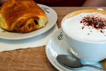 chocolate croissant and white coffee on a plate in a a bakery - traditional french breakfast in Paris, France