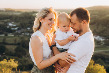 Fototapeta premium Loving Family Embracing Outdoors During Golden Hour with Young Child in Beautiful Scenic Landscape