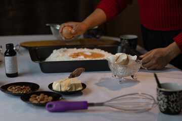 Unrecognizable brown skin woman cracking an egg and mixing it with flour, butter, nuts, vanilla and kitchen utensils ready to prepare the dough.