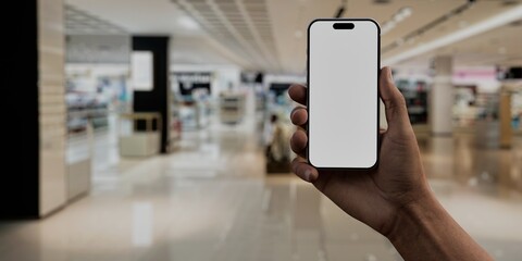 Asian male using smartphone with a blank white screen. Shopping mall, interior, cosmetic counters apps mockup. Vertical phone orientation