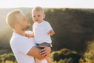 Fototapeta premium Father Holding Baby Outdoors in Nature During Sunset, Expressing Bond and Affection