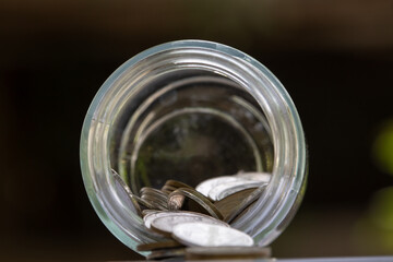 Loose coins scattered from a tipped-over jar, representing financial challenges, savings, and expenses.