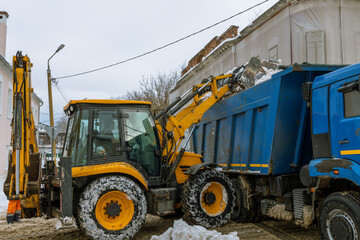 A yellow and blue construction vehicle is dumping snow