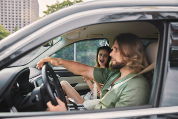 A young man driving a car while a woman in the passenger seat smiles excitedly Urban background with green trees Natural lighting creates a vibrant atmosphere