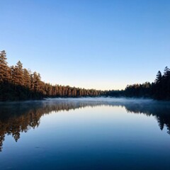Fototapeta premium a serene lake surrounded by towering pine trees with mist rising from the water as the sun begins