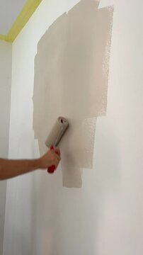 Painting wall with beig paint using roller. Construction worker, tool, apartment renovation.