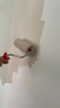 Painting wall with beig paint using roller. Construction worker, tool, apartment renovation.