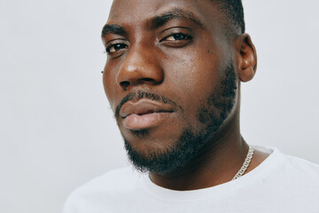 Obraz premium Portrait of a confident young man with a serious expression, wearing a simple white t shirt against a subtle light background, showcasing a modern and stylish vibe