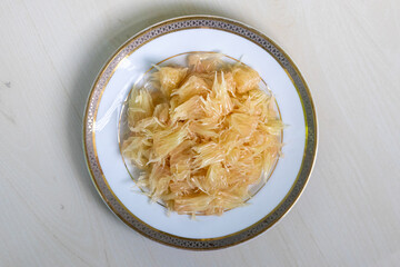 Fresh, peeled pomelo fruit flesh in a white plate on a wooden background. Its scientific name is Citrus maxima or Citrus grandis. In Bangladesh, it is locally called jambura. Top view.
