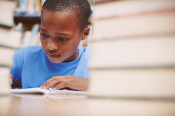 Black child, writing and study in library for education, knowledge or academic opportunity at elementary school. Young boy, learning or books on table for lesson, growth and progress in assessment