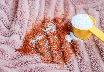 Close up of washing powder and a dirty pink towel with red stain on grey table. Cloth stain remover concept