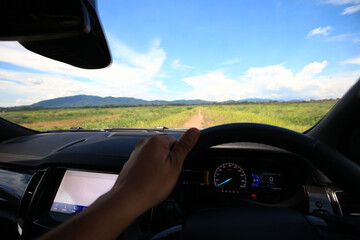 A car driving through a scenic countryside road with mountains in the background and a clear blue sky