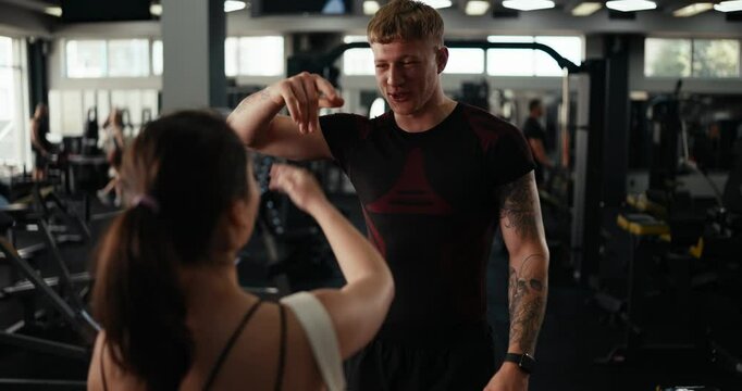 Rear view of a happy girl gym client saying hello to her trainer guy before starting a workout and fitness class in the gym